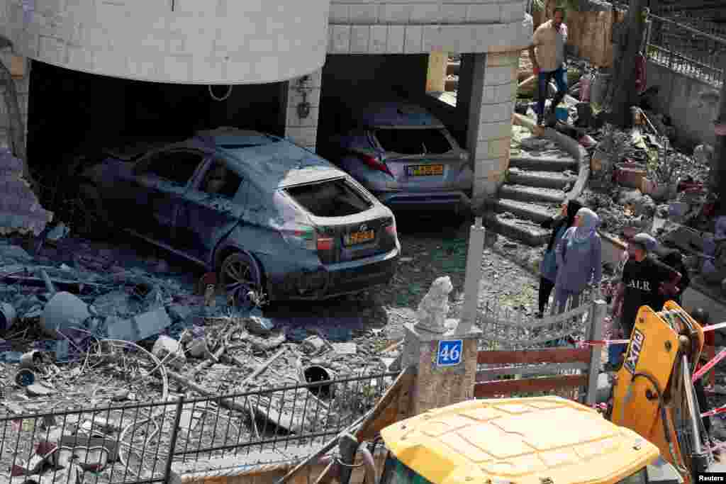 Люди стоят возле поврежденных автомобилей после того, как ракеты, выпущенные из Ирана, попали в жилой дом, в Тамре, Израиль, 15 июня 2025 года. REUTERS/Ammar Awad