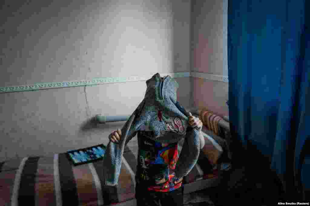 Руслан, 9-річний переселенець із Торецька, одягається тепліше у притулку, де він зараз проживає. Сім&#39;ї з дітьми зазвичай залишаються в притулку для внутрішньо переміщених осіб на кілька днів, тоді як літні евакуйовані, яким важче знайти постійне житло, іноді перебувають там місяцями