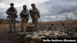 Бійці спецпідрозділу з розмінування Нацполіції стоять біля знешкоджених протитанкових мін під час операції з розмінування біля міста Ізюм, Харківська область, Україна, 24 жовтня 2023 року