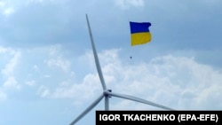 Український прапор в небі поблизу вітрової турбіни Тилігульської вітрової електростанції в Миколаївській області, відкритій в час війни. Екологи закликають Київ робити більший акцент на вітрових елекстростанціях (ВЕС). 19 травня 2023 року