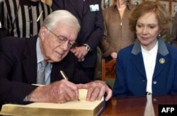 جیمی کارتر در کنار همسرش رزالین هنگام امضای کتاب یادبود مهمانان در مؤسسه نوبل در اسلو، دسامبر۲۰۰۲