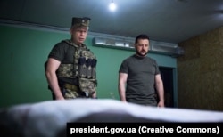 Тоді командувач Сухопутних військ ЗСУ Сирський (ліворуч) доповідає Зеленському на позиції біля лінії фронту на Донеччині, 26 червня 2023 року
