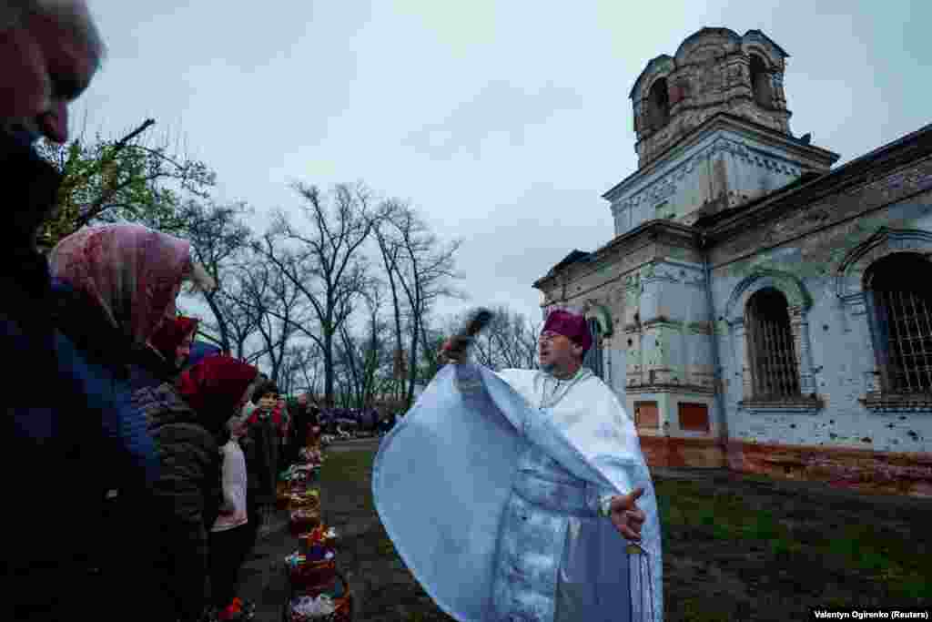 Отець Сергій кропить вірян свяченою водою на Великдень біля&nbsp;знищеної рік тому, внаслідок масштабного вторгнення армії РФ, церкви у селі Лукашівка Чернігівської області, 16 квітня 2023 року
