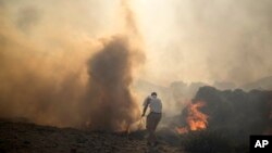 Жергиликтүү тургун Родос аралындагы Линдос курорттук жайына жакындаган өрттү өчүрүү аракетин көрүп жатат. Грекия. 24-июль, 2023-жыл. 