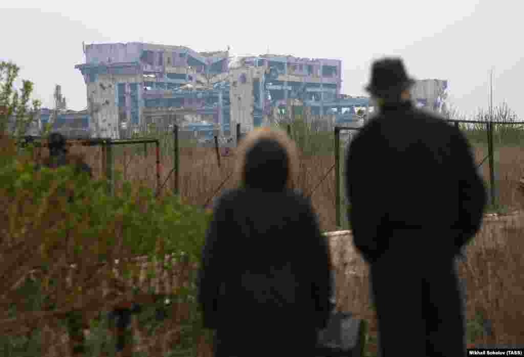 Пожилая пара смотрит на руины аэропорта, апрель 2017 года. В феврале 2022 года Кремль начал полномасштабное вторжение в Украину, к ноябрю вся территория разрушенного аэропорта перешла под контроль российских войск