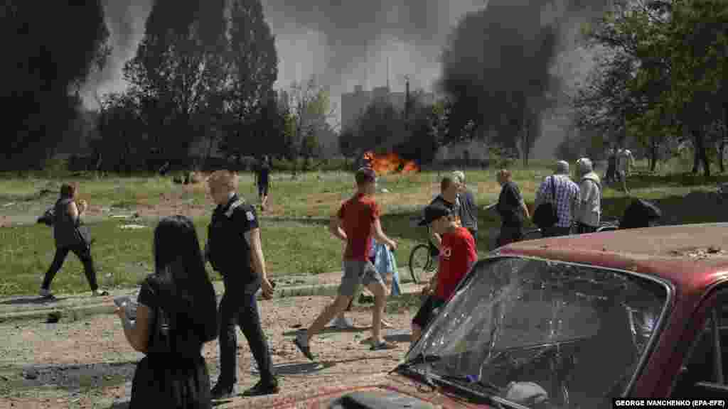 Locals react at the scene as cars burn nearby.