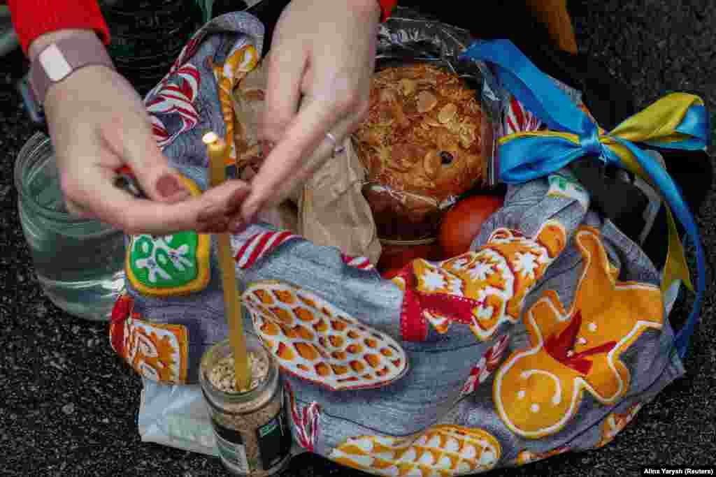 Жінка запалює свічку у великодньому кошику під час богослужіння у Володимирському кафедральному соборі в Києві, 16 квітня 2023 року&nbsp;