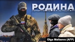 Биз коргоп жаткан мекен" деп жазылган сүрөттүн алдынан өтүп бараткан кишилер.