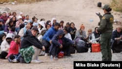 ABŞ hərbçisi əsas və ikinci dərəcəli sərhəd çəpərləri arasında toplaşan miqrantlarla danışır.