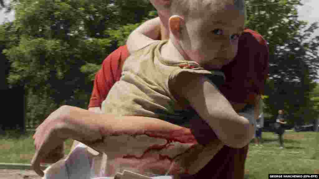 An injured young boy carries a toddler away from a residential building.