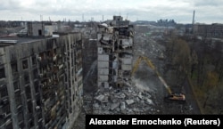 Екскаватор зносить зруйнований багатоповерховий житловий будинок в окупованому Маріуполі, 15 лютого 2023 року