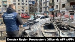 A war crimes prosecutor stands next to destroyed cars in the courtyard of a damaged residential building following a missile attack in Myrnohrad, Donetsk region, Ukraine, on March 10.