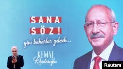 زنی در حال کار با تلفن همراه در مقابل پوستر بزرگ تبلیغاتی کمال قلیچداراوغلو