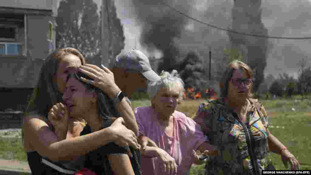 A young girl is comforted by a woman as others help an elderly woman as cars burn in the background. Regional Governor Oleh Synehubov said a Russian Iskander missile had slammed into a residential area in Pervomayskiy.