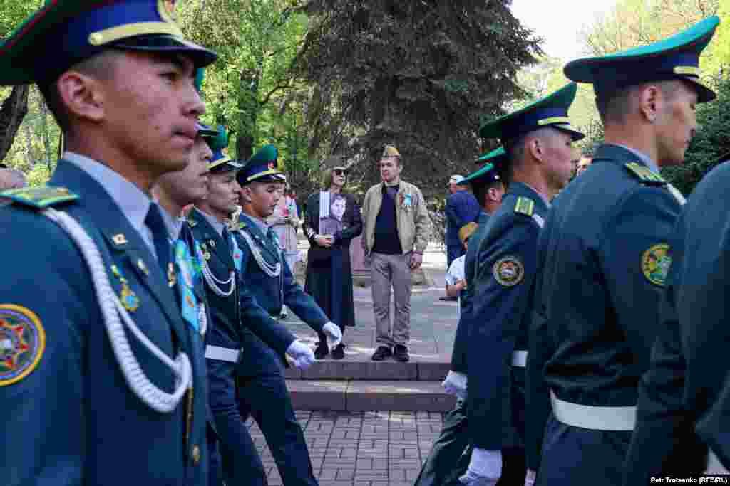Мужчина и женщина в военной атрибутике наблюдают за марширующими военными