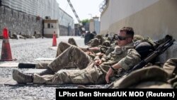 Кабул әуежайынан дипломаттар мен өзге де адамдарды эвакуациялауға жәрдемдесуге барған Ұлыбритания сарбаздарының демалып отырған сәті. 2021 жылғы 23 тамызда Reuters агенттігі жариялаған сурет.