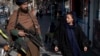 A woman walks past a Taliban fighter in Kabul on December 26.
