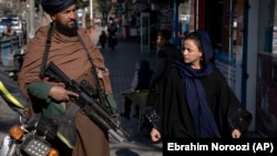 A woman walks past a Taliban fighter in Kabul on December 26.