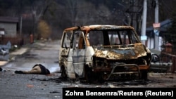 Цела забітага расейскімі вайскоўцамі мірнага жыхара і спаленая машына на вуліцы Бучы. 2 красавіка 2022 году