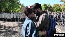 Молодая пара активистов на фоне колючей проволоки и полицейского кордона вскоре после столкновений между демонстрантами и правоохранителями в Ереване, 16 апреля 2018 г.