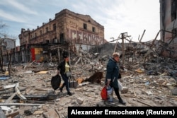Жінки із важкими сумками пробираються руїнами Маріуполя, у якому російська армія знищила понад 90% усіх будинків. 10 квітня 2022 року