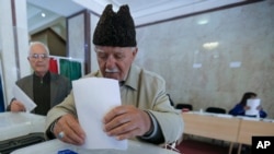 Пожилой избратель опускает бюллетень в урну в день президентских выборов. Баку, 11 апреля 2018 года.