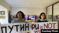 Активистки Айнур Абсеметова и Дана Жарикова показывают плакат, с которым планировали выйти на акцию протеста у консульства России в Алматы. 12 октября 2022 года