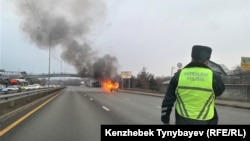 Жол үстінде жанып жатқан автокөлікке қарап тұрған полиция қызметкері. Алматы, 8 желтоқсан, 2021 жыл. Азаттық архивіндегі фото