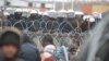 Мігранти на білорусько-польському кордоні перед парканом і польськими військовослужбовцями