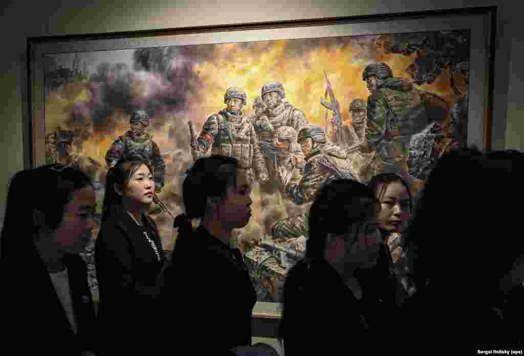 گردشگران کره شمالی از کنار یک تابلوی نقاشی با عنوان «مبارزان قهرمان برای عزت و افتخار میهن» عبور می‌کنند. گنبدهای بنایی که به نظر می‌رسد یک کلیسای ارتدکس باشد در بالا، سمت چپ، قابل مشاهده است.