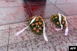 Вянкі, ускладзеныя актывістамі, адзін у памяць ахвяраў Смаленскай катастрофы і адзін у памяць ахвяраў кліматычных зьменаў, на бруку з чырвонымі плямамі, якія імітуюць кроў каля помніка ахвярам Смаленскай трагедыі 2010-га ў Варшаве, 9 красавіка 2025 году