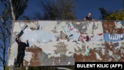 Молодые люди снимают транспаранты периода российской оккупации в недавно освобожденном Херсоне 14 ноября 2022 года