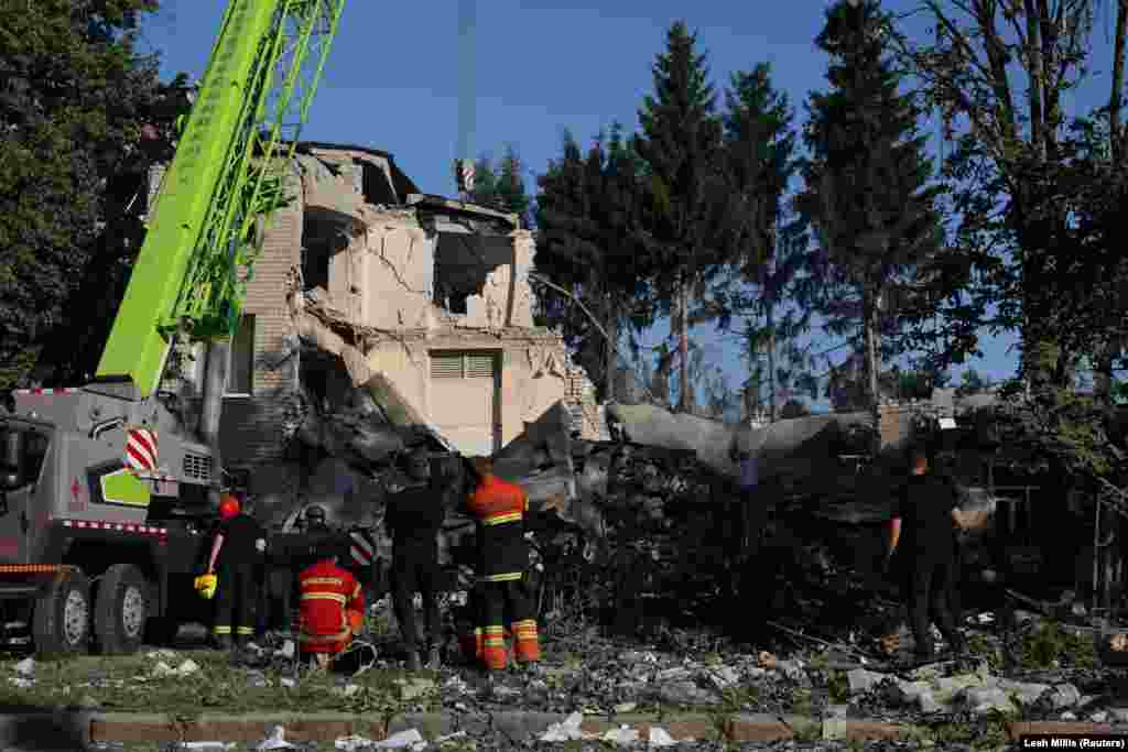 Пожежники спостерігають за роботою крана, після того, як загасили пожежу, що виникла внаслідок російського нічного обстрілу школи у Харкові, 4 липня 2022 року