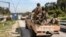 SYRIA - Security forces loyal to the interim Syrian government ride in the back of a vehicle moving along a road in the western city of Latakia on March 9, 2025. 