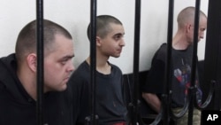 Британці Ейден Еслін (ліворуч), Шон Піннер (праворуч) та громадянин Марокко Брагім Саадун (посередині) у так званому «суді» проросійського угруповання «ДНР». Окупований Донецьк, 9 червня 2022 року 