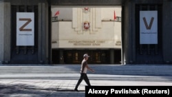 Aqmescit şeeriniñ sakini Rusiyeniñ Ukrayinağa qarşı ücümini timsal etken levhalar olğan Qırım parlamentiniñ binası ögünden keçe. Aqmescit, 2024 senesi sentâbrniñ 27-si