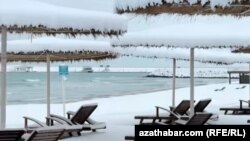 Hazar deňziniň ýakasyndaky Awaza syýahatçylyk zolagyna düşen gar plýažlarda oturdylan günden goraýjy saýawanlaryň üstüni örtdi. 24-nji fewral, 2025 ý. Awaza, Türkmenistan.
