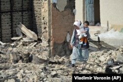 Киргизька жінка з дитиною на руках проходить через руїни свого будинку в селі Максат біля киргизько-таджицького кордону, 4 травня 2021 року