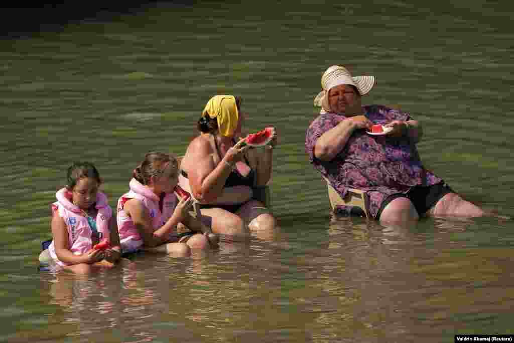 Люди охлаждаются и едят арбуз в реке Эреник во время жары, недалеко от Гьяковы, Косово, 25 июня 2025 года. REUTERS/Вальдрин Кшемай