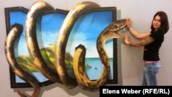 Координатор выставки 3D-картин Екатерина Литвинова демонстрирует посетителям, как выбрать правильный ракурс, чтобы на фотографии был отчетливо виден эффект трехмерного изображения. Караганда, 6 августа 2014 года. 