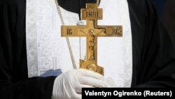 Священник Православної церкви України (ПЦУ) в захисних рукавицях (в час епідемії коронавірусу) під час освячення пасок для відправлення їх українським бійцям на лінію фронту. Київ, 13 квітня 2020 року 