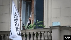 An official uses his smartphone next to the flag of the Islamic Emirate of Afghanistan at the balcony of the Afghan Embassy in Moscow on July 4.