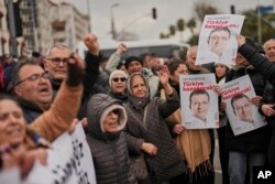 Vatan қауіпсіздік департаменті алдына жиналған жұрт Стамбұл мэрі Екрем Имамоглудың суретін мен ұраны жазылған плакат ұстап тұр. Имамоглуды осы ғимаратқа әкелмекші деген хабар тараған еді.