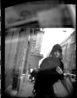 Молода жінка тісніше кутається в своє пальто, коли проходить повз таємного агента з камерою в центрі Праги