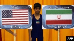 یک کودک ورزشکار ایرانی بین پلاکارد‌های تیم‌های کشتی ایران و آمریکا در بیست و نهمین دوره مسابقات جام تختی در تهران