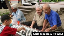 11-летний Досбулат Жупархан "во дворе дяди Казиса" играет в шахматы с мастером спорта по шахматам Александром Синявским (рядом с ним любитель игры в теннис и шахматы Анатолий Авдеев). Алматы,  6 июня 2010 года. 