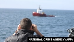 Жээкте дүрбү салып турган Британиянын кылмыштуулукка каршы агенттигинин кызматкери Иллюстрациялык сүрөт.