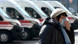 Женщина в маске на фоне машин скорой помощи в центре Киева.