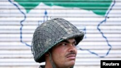 یک سرباز ارتش هند در مقابل نقشه‌ای از کشمیر روی کرکرۀ یک مغازه
