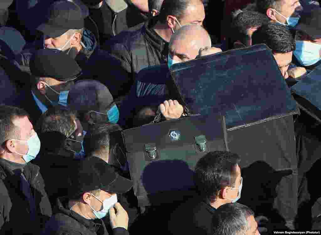 Bodyguards screen Armenian Prime Minister Nikol Pashinian with ballistic shields as he enters Yerablur cemetery on December 19. Pashinian faced anger from many in the grieving crowds who shouted, &quot;Nikol, you traitor!&quot;&nbsp;